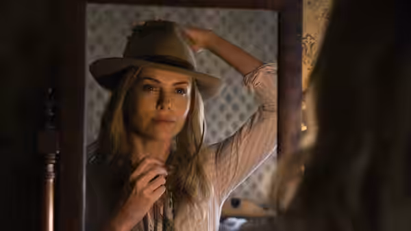 Anna adjusts her hat while looking into a mirror