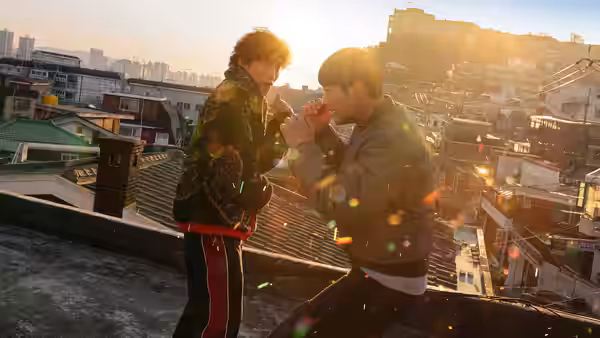 Two men face each other on a rooftop above the city at sunset
