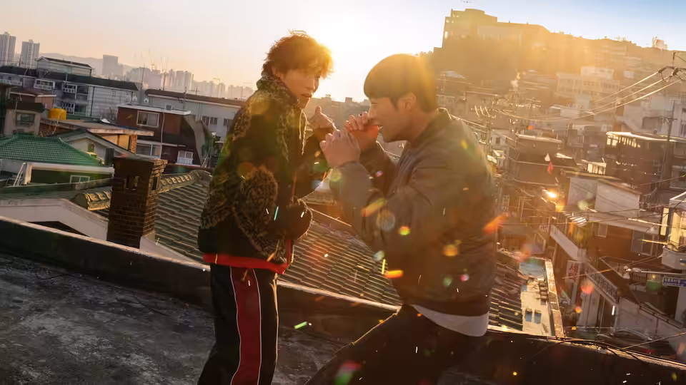 Two men face each other on a rooftop above the city at sunset