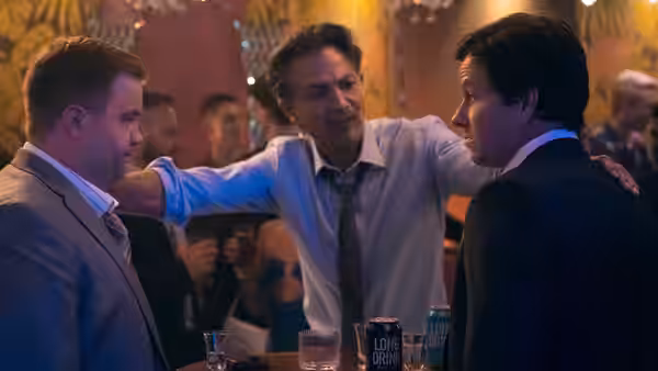 A man in a white shirt embraces two suited men at a crowded bar