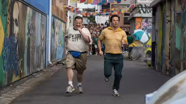 Brad (Mark Wahlberg) and Elijah (Paul Walter Hauser) run down a decorated city street