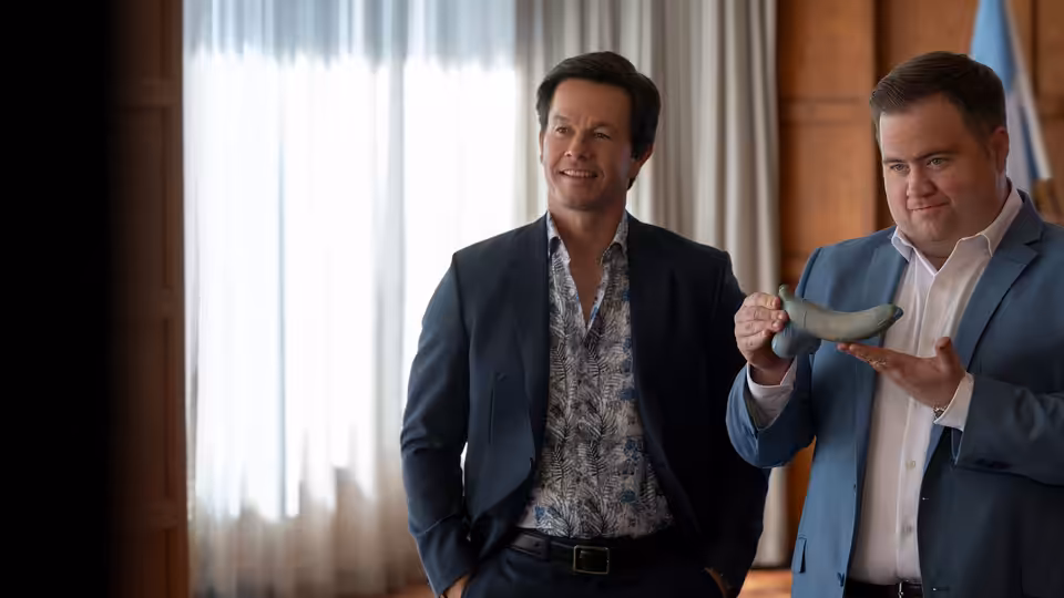 Brad (Mark Wahlberg) holds a small object while Elijah (Paul Walter Hauser) smiles beside him