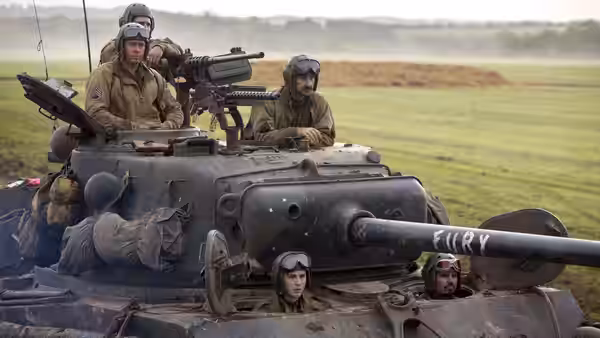 Soldiers ride atop an armored tank crossing open fields