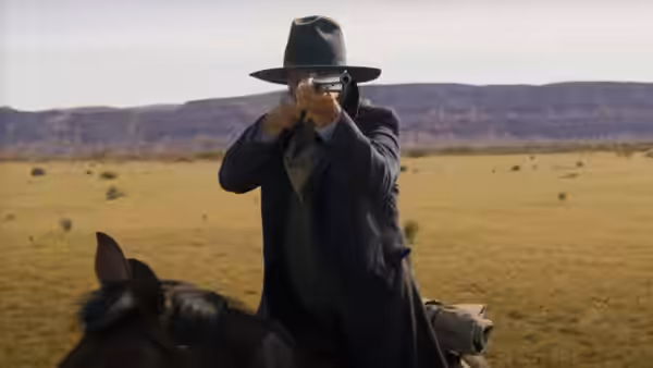 Hayes Ellison (Kevin Costner) raises a pistol while mounted on horseback in the open range
