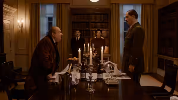 Two officials face each other across a candlelit dining table in a library