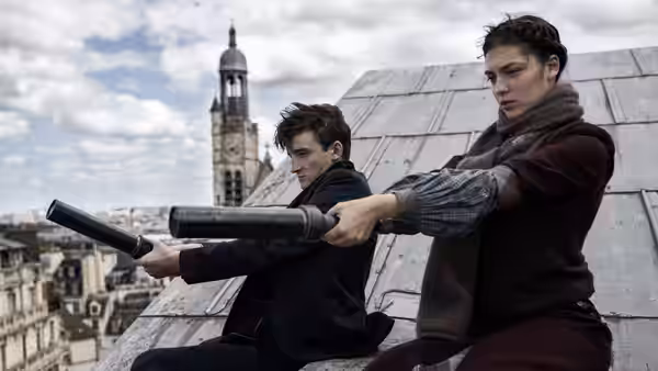 Two young men crouch on a rooftop, aiming launchers across the city