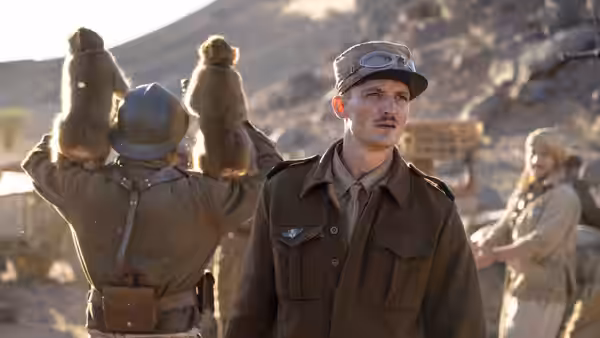 A uniformed officer watches as a soldier raises two objects in the air