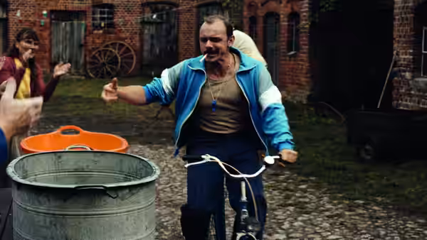A man straddles a bicycle and gestures to a woman outside a brick building
