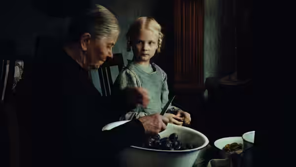 An older man sits beside a little girl, handling an object over a washbasin
