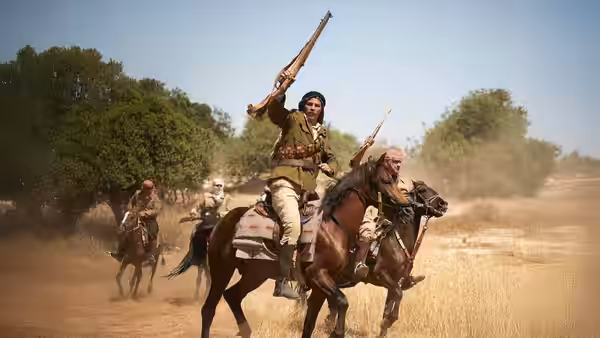 Armed riders on horseback gallop across a dusty field