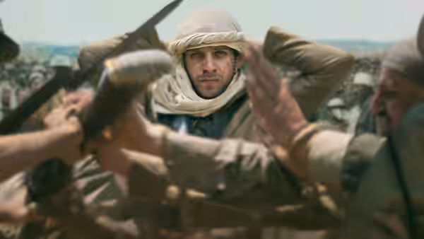 Soldiers adjust a man's headwrap as he faces forward among a crowd