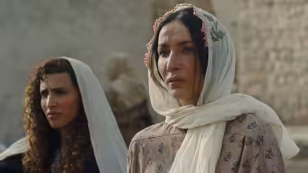 Two women in white headscarves stand together outside a stone building