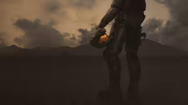 An armored Spartan holds a glowing orange device against a dark, open landscape
