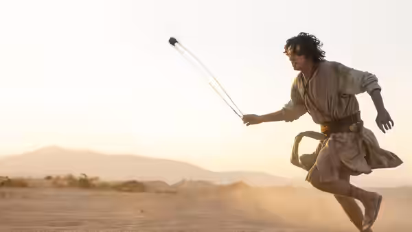 A young shepherd runs across the open ground, swinging a sling
