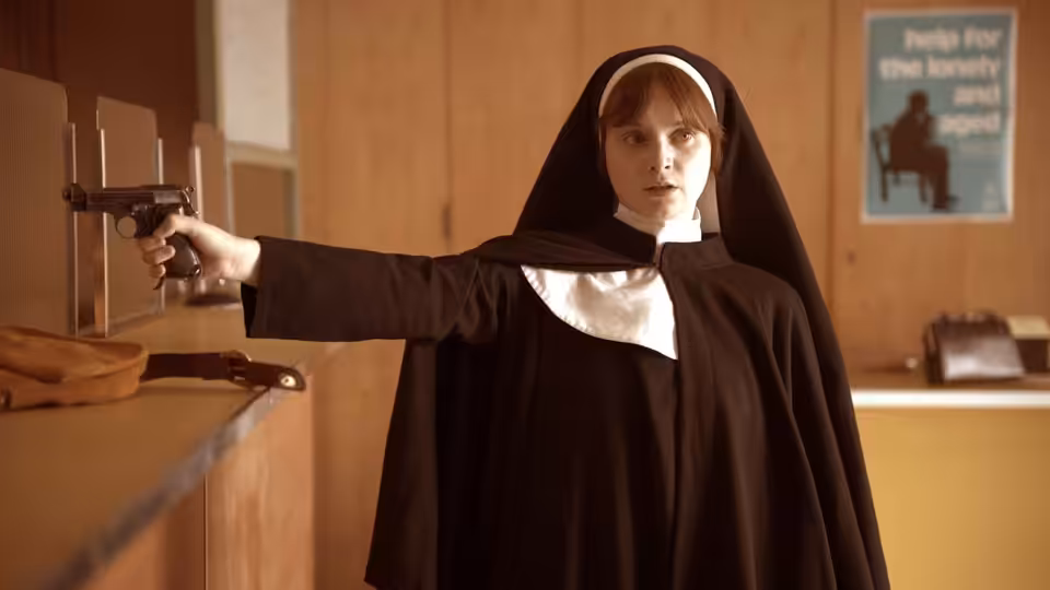 Dolours Price (Lola Petticrew) aims a handgun across a room in a nun’s habit