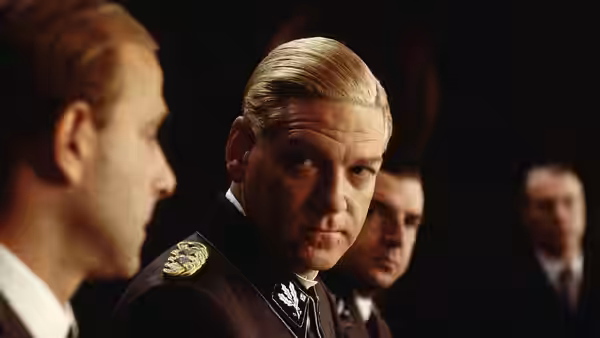Reinhard Heydrich (Kenneth Branagh) turns toward another official during a meeting