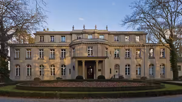 A stately villa stands behind a circular garden and bare trees
