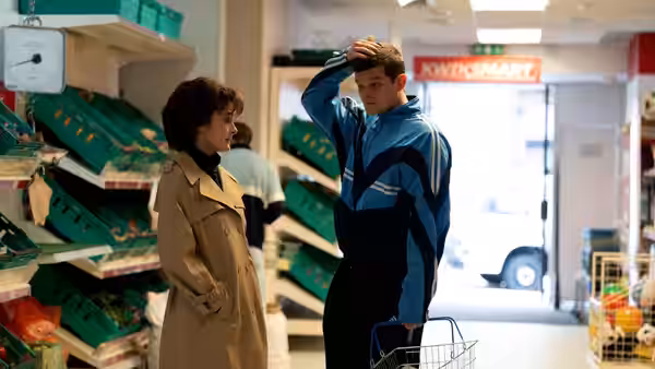 John (Robert Aramayo) stands beside a woman in a supermarket aisle, holding his head
