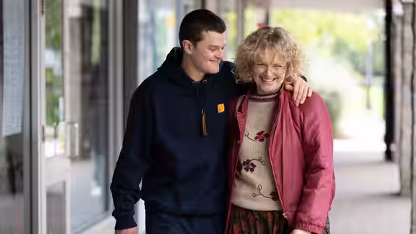 John (Robert Aramayo) walks with his arm around a smiling older woman