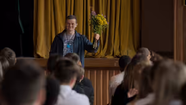 A man holds a bouquet onstage as an audience watches