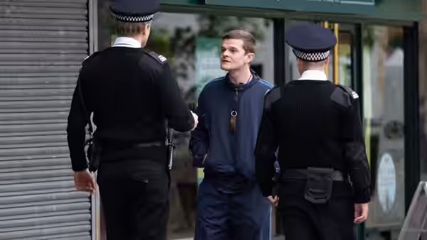 John (Robert Aramayo) talks with two uniformed officers outside a building