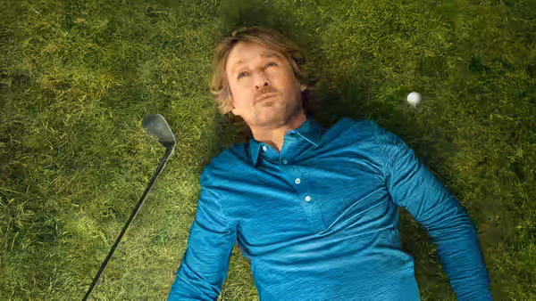 Pryce Cahill (Owen Wilson) lies on the grass beside a golf club and ball