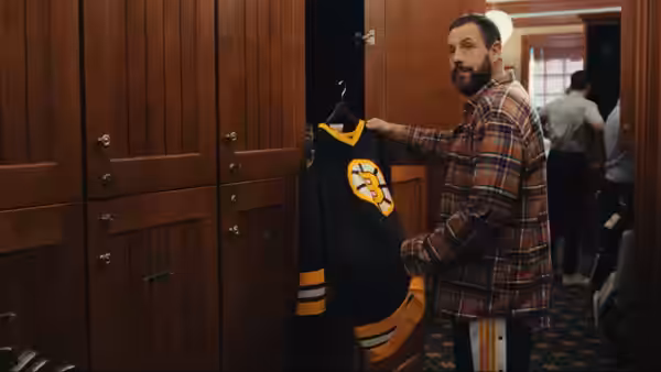 Happy Gilmore (Adam Sandler) holds up a hockey jersey beside open lockers