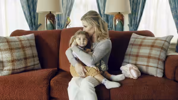 Virginia (Julie Bowen) cuddles a baby on a living room sofa