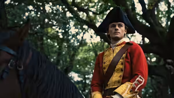 George Washington (William Franklyn-Miller) stands beside his horse in a red uniform
