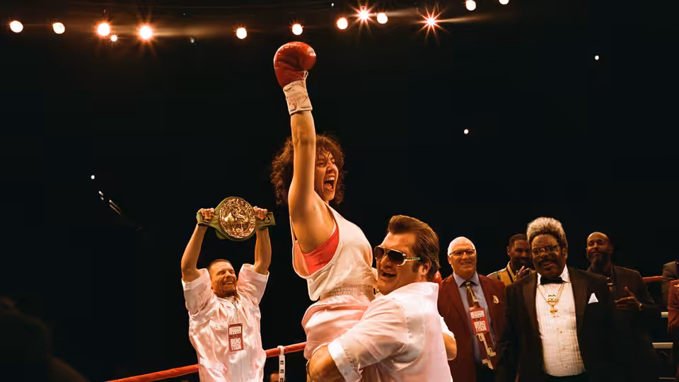 Christy Martin (Sydney Sweeney) raises a gloved fist in the boxing ring as officials watch