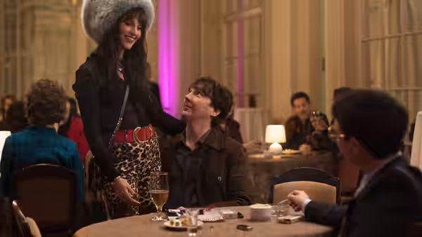 A woman in a fur hat stands beside a seated man at a restaurant table