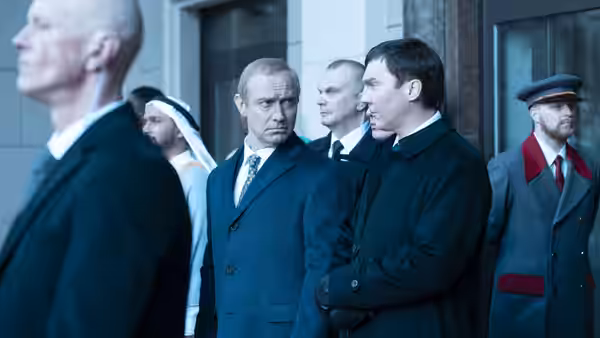 Vladimir Putin (Jude Law) stands among suited men outside a building