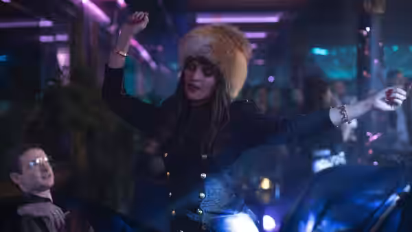 A woman in a fur hat dances beneath neon lights in a club