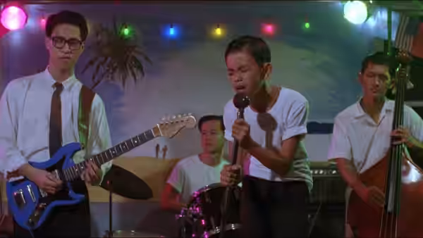 A young singer performs with a band beneath colored lights