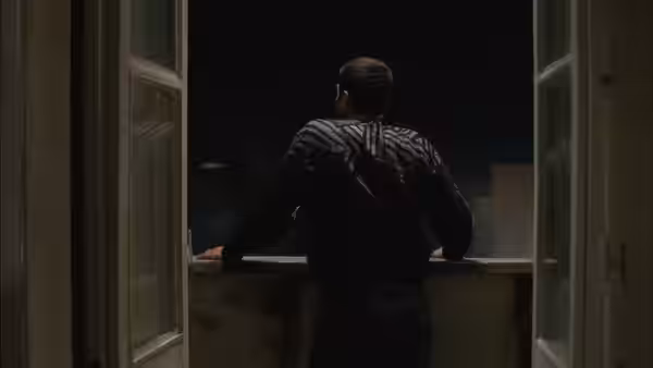 A man leans on a windowsill, looking out into the darkness