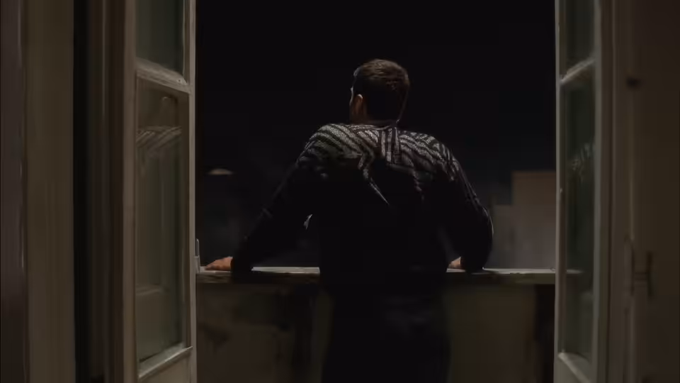 A man leans on a windowsill, looking out into the darkness