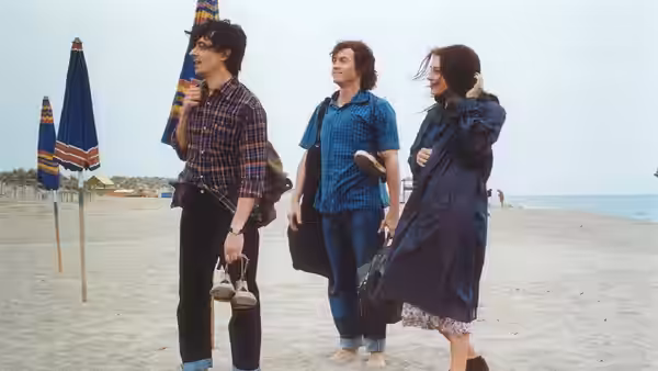 Three young people walk together along a beach lined with umbrellas