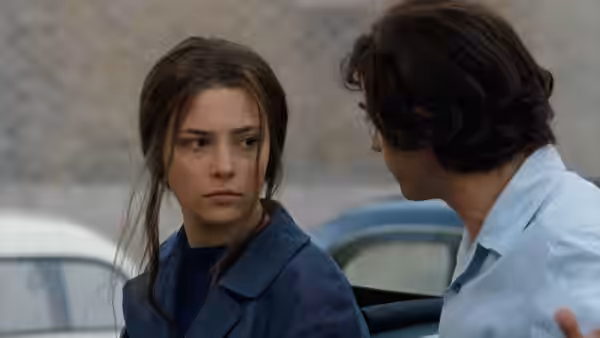 A young woman sits beside a dark-haired man near a parked car