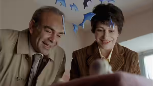 An older man and woman smile down at a baby beneath hanging decorations