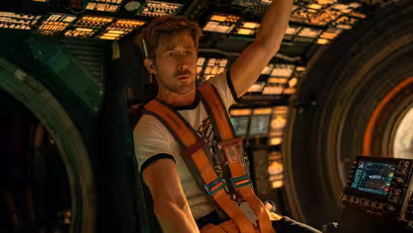 Ryan Gosling as Ryland Grace reaching upward in a spacecraft cockpit