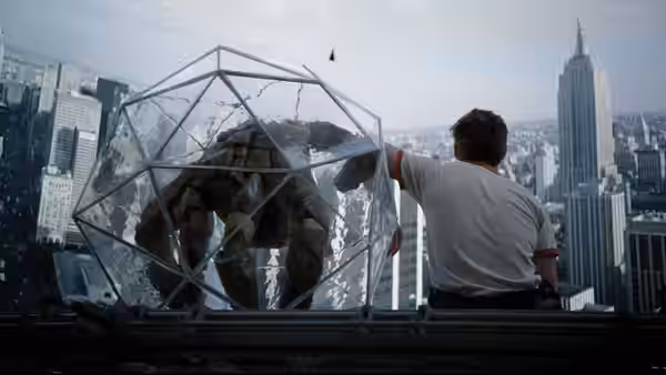 A man and an alien inside a transparent enclosure on a city rooftop
