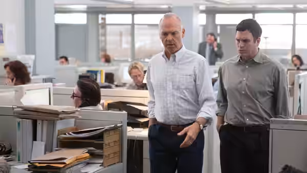 Two men walk through a large open-plan newsroom filled with desks