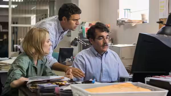 Three colleagues examine a computer screen together in an office