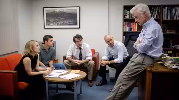 Five people sit in a meeting around a small table in an office