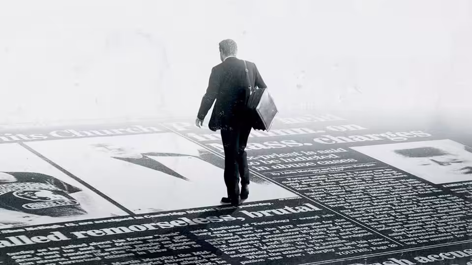A man in a suit walks over large newspaper pages on the floor