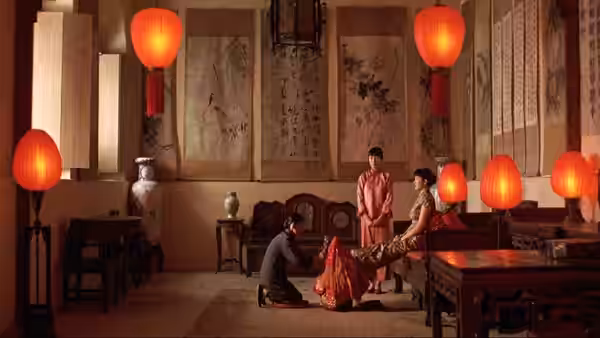 a man kneeling before two women in a lantern-lit hall