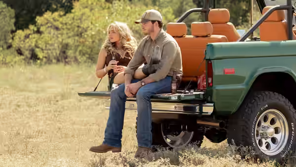 A blonde woman sits beside a man on a pickup truck tailgate