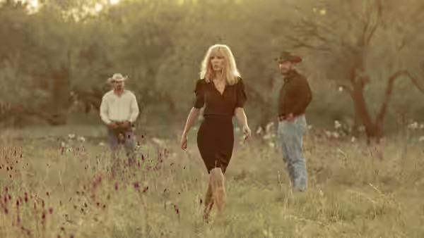 Beth Dutton (Kelly Reilly) walks through a meadow as two men watch