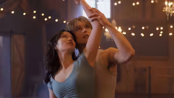 A young couple practice a raised-arm skating pose beneath warm lights