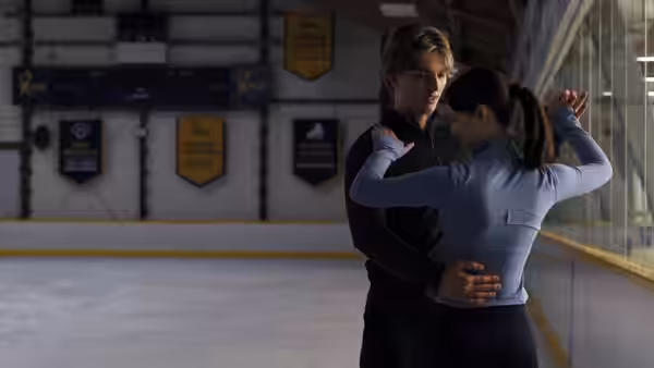 A skating pair practice a close hold beside the rink boards